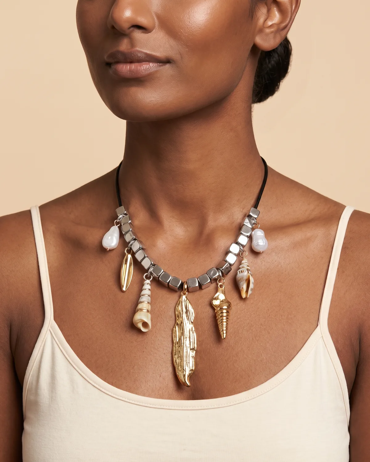 Island Nomad: a black cord base threaded with chunky silver cube beads, adorned with an array of dangling pendants including baroque pearls, a natural seashell, and various polished gold organic and shell-shaped charms.