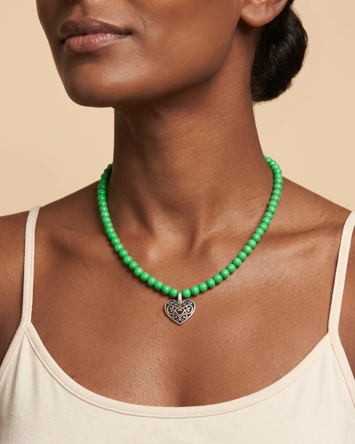 Jade Devotion: a single strand of small, vibrant green round beads accented with a central, antiqued silver heart pendant with an intricate filigree design.