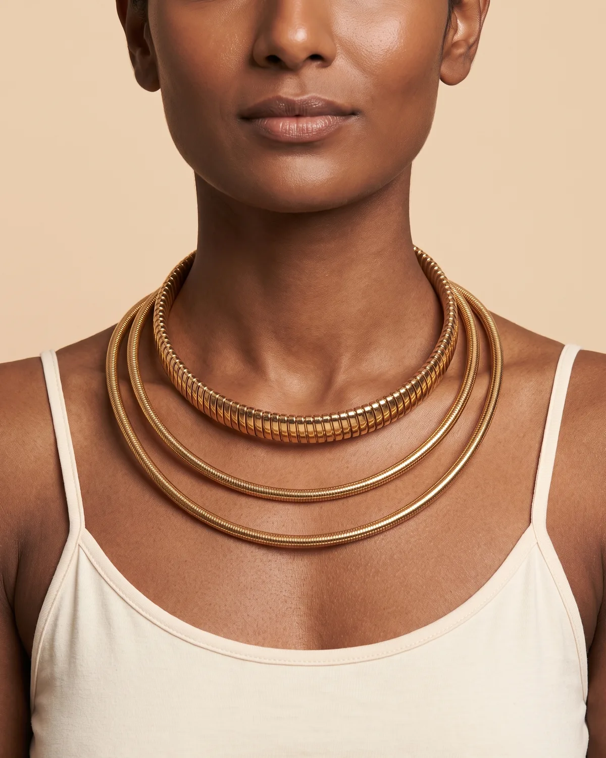 layered Collar: a layered set of three metallic gold choker necklaces, highlighted by a prominent top strand composed of flexible, ribbed segments and paired with two thinner, smooth omega-style bands below.