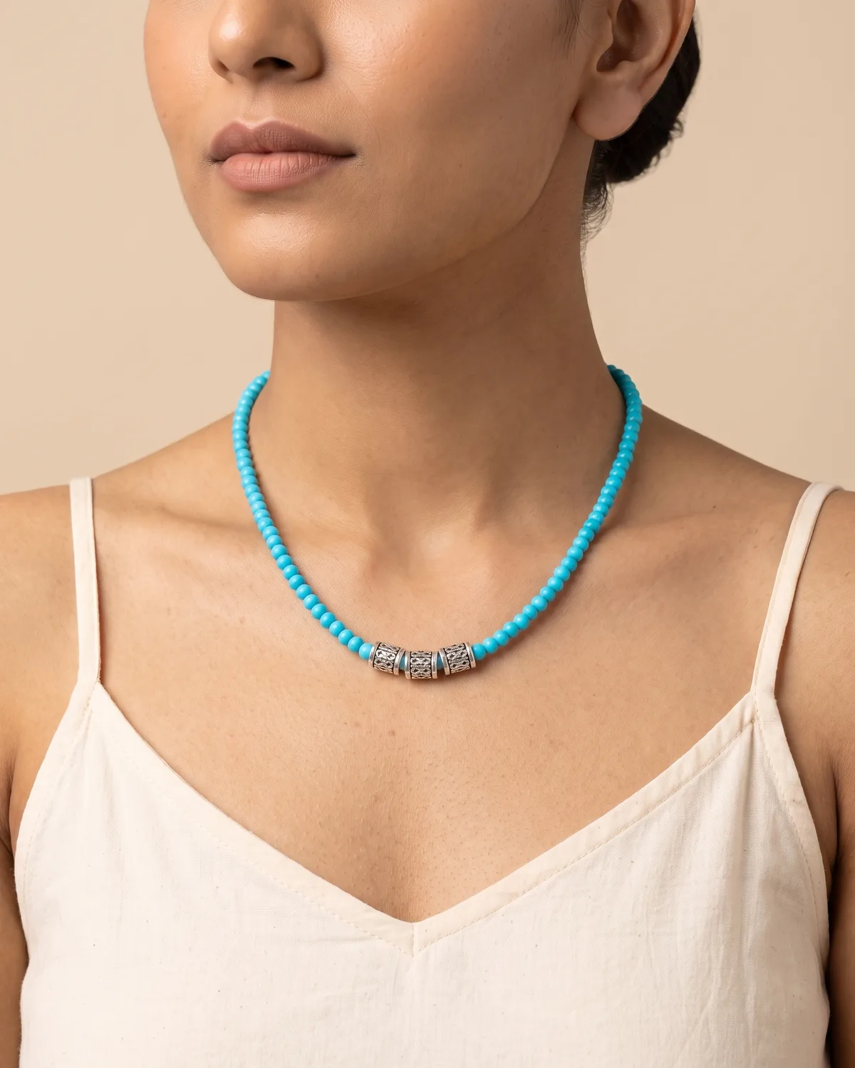 Ocean Whispers: a single strand of small, vibrant turquoise-blue round beads centered with three patterned, cylindrical silver spacer beads.