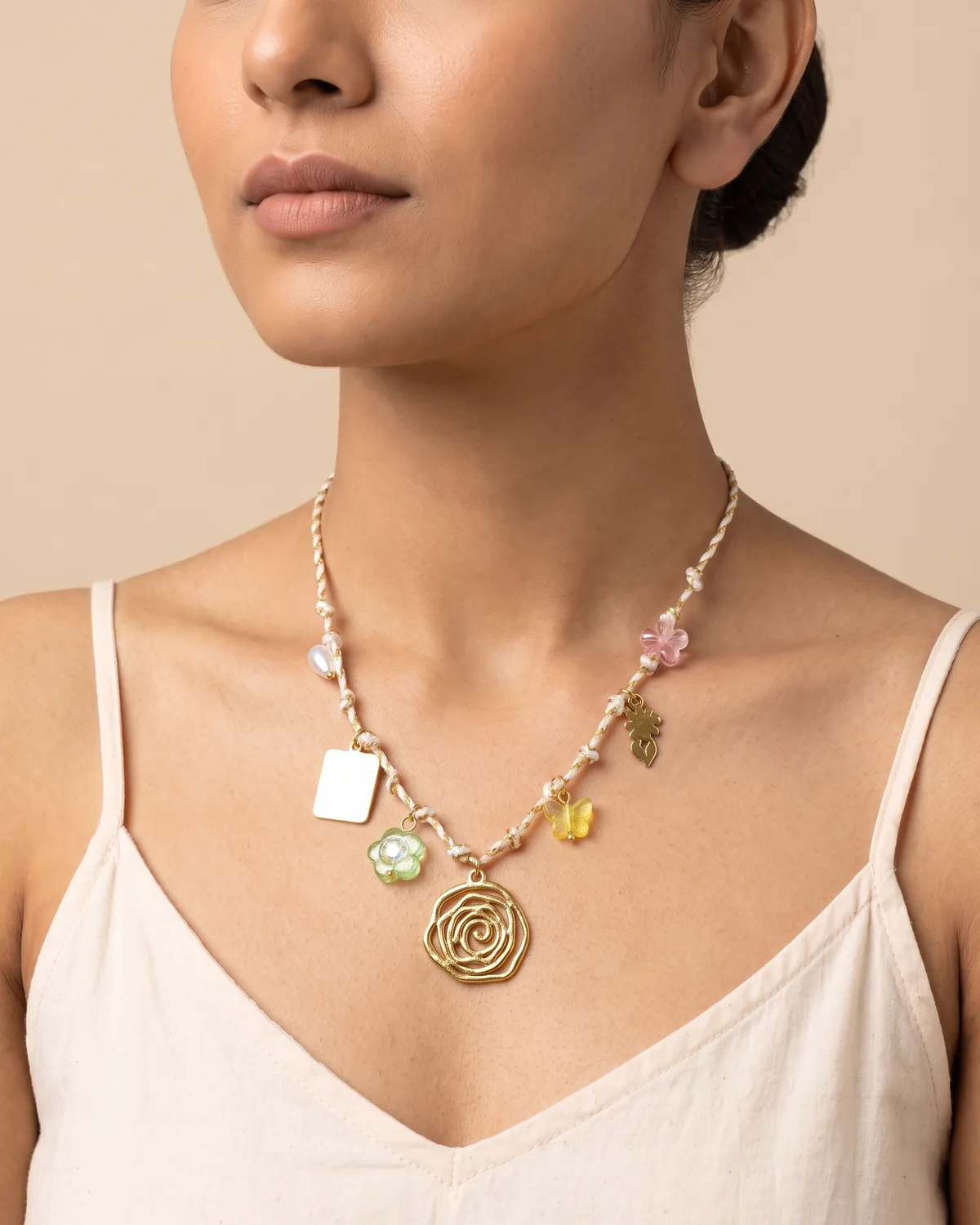 Rosebud Scarf: a slender white and gold braided cord beautifully adorned with an openwork rose pendant, a smooth square tag, and assorted pastel accents including a green flower and a yellow butterfly.
