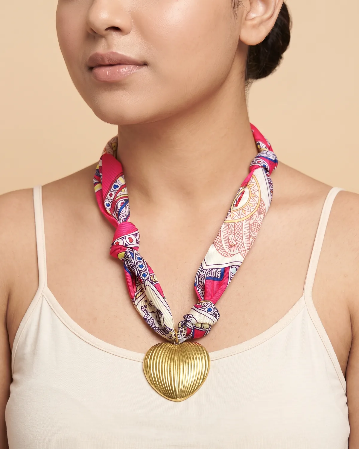 Sweetheart Scarf: A textured, gold-toned heart pendant suspended from a vibrant, knotted fabric ribbon with colorful bohemian and paisley patterns.